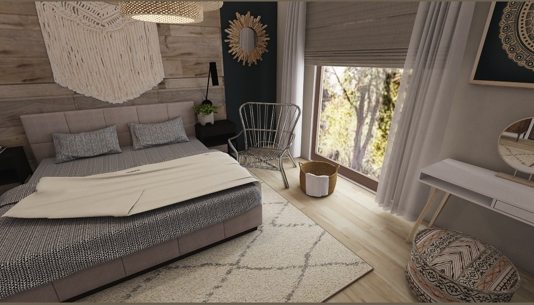 Sypialnia w neutralnych barwach z łóżkiem z szarą pościelą, makramą nad wezgłowiem i okrągłym lustrem z drewnianymi elementami na ścianie, uzupełniona metalowym krzesłem i pufem.