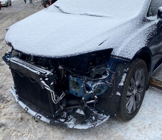 Uszkodzony przód niebieskiego samochodu osobowego, pokryty śniegiem, z widocznym radiatorem i elementami konstrukcyjnymi, na zimowym tle.