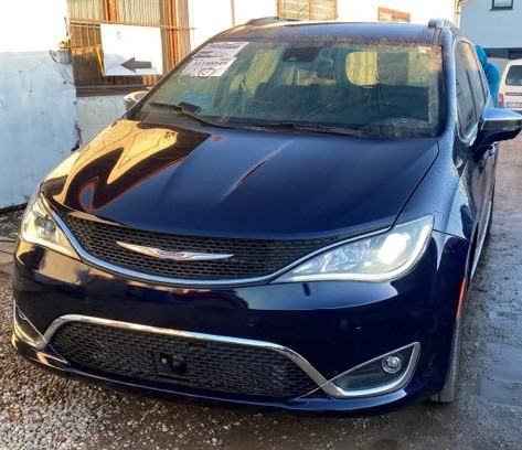 Niebieski minivan Chrysler Pacifica z widoczną naklejką informacyjną na przedniej szybie, zaparkowany na zewnątrz warsztatu.