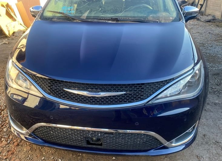 Przód granatowego samochodu Chrysler Pacifica z uszkodzoną szybą przednią, widoczne pęknięcia i ślady po uderzeniu.