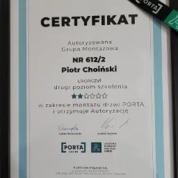 Oprawiony certyfikat autoryzacji montażu drzwi PORTA dla Piotra Choińskiego, ukończony drugi poziom szkolenia, z podpisami Łukasza Wawrzyńskiego i Szymona Kwaśnika, uzupełniony o smyczkę z logo PORTA.