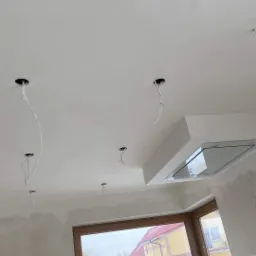 Przygotowany sufit i ściany pod wykończenie: widoczne otwory na oświetlenie z wystającymi przewodami, fragment okapu kuchennego, ściany z widocznymi śladami po szpachlowaniu i gładziowaniu.