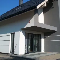 Dwukolorowa elewacja domu jednorodzinnego z grafitową dachówką i szarymi ramami okiennymi, widok z zewnątrz na fragment budynku z widocznymi detalami wykończenia.