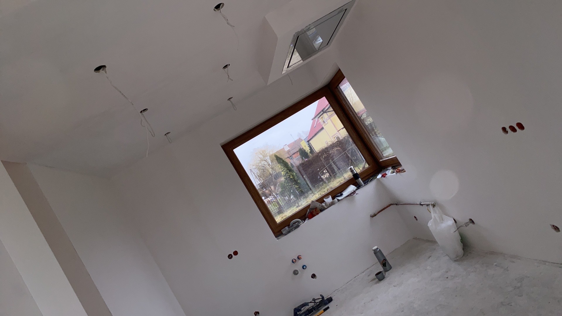 Pokój po remoncie, widoczne gładkie, białe ściany, okno dachowe, instalacja elektryczna w suficie i ścianach, oraz narzędzia na podłodze.