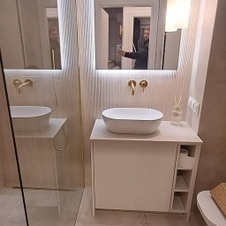 Dizajn Jarosław Lauer - Nowoczesna łazienka z umywalką nablatową, lustrem z podświetleniem LED i złotą armaturą. Widoczne płytki z delikatnym wzorem i minimalistyczne oświetlenie.