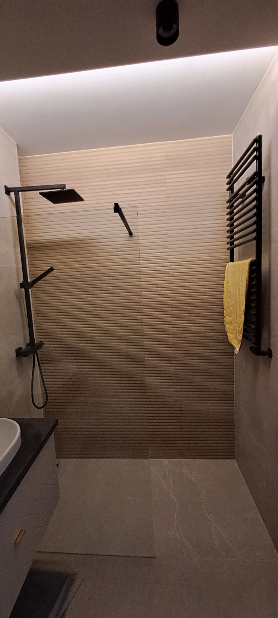 Nowoczesna łazienka z czarną armaturą: deszczownica, grzejnik drabinkowy z ręcznikiem, umywalka z szafką. Płytki ścienne z efektem ombre. Minimalistyczny design.