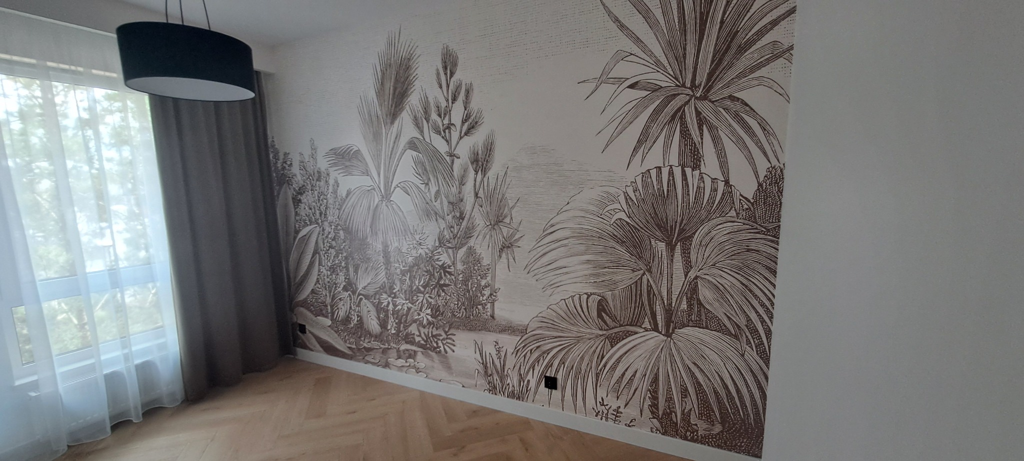 Wykończone wnętrze z fototapetą w stylu retro z motywem tropikalnych roślin, drewnianą podłogą i czarną lampą wiszącą. Widok na okno z zasłonami.