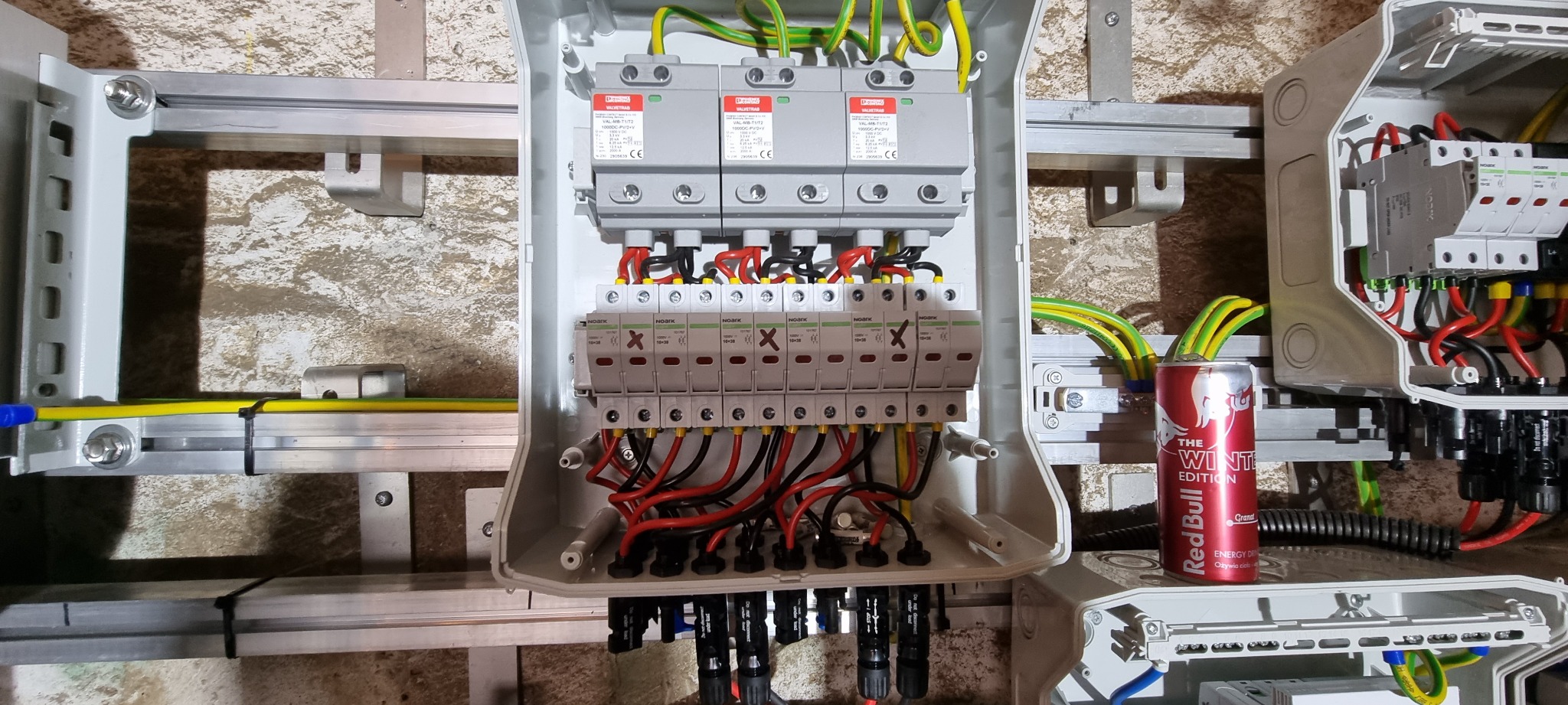 Rozdzielnica elektryczna z zabezpieczeniami przepięciowymi, zamontowana na szynie, z puszką Red Bull The Winter Edition stojącą obok.