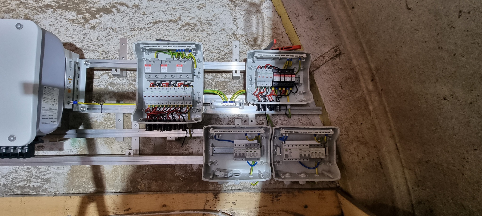 Szare skrzynki elektryczne z okablowaniem i zabezpieczeniami zamontowane na szynie, część instalacji w surowym pomieszczeniu.