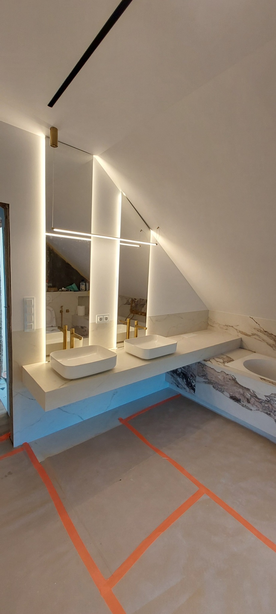 Nowoczesna łazienka na poddaszu z dwoma umywalkami nablatowymi, lustrem z podświetleniem LED i marmurowym blatem. Podłoga zabezpieczona taśmą malarską.