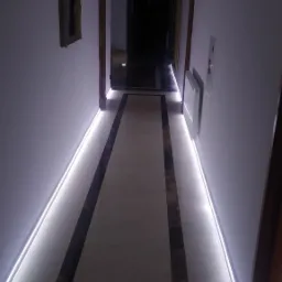 Długi korytarz z marmurową podłogą i oświetleniem LED wzdłuż ścian, zakończony ciemnym przejściem. Na ścianie wisi rama obrazu.