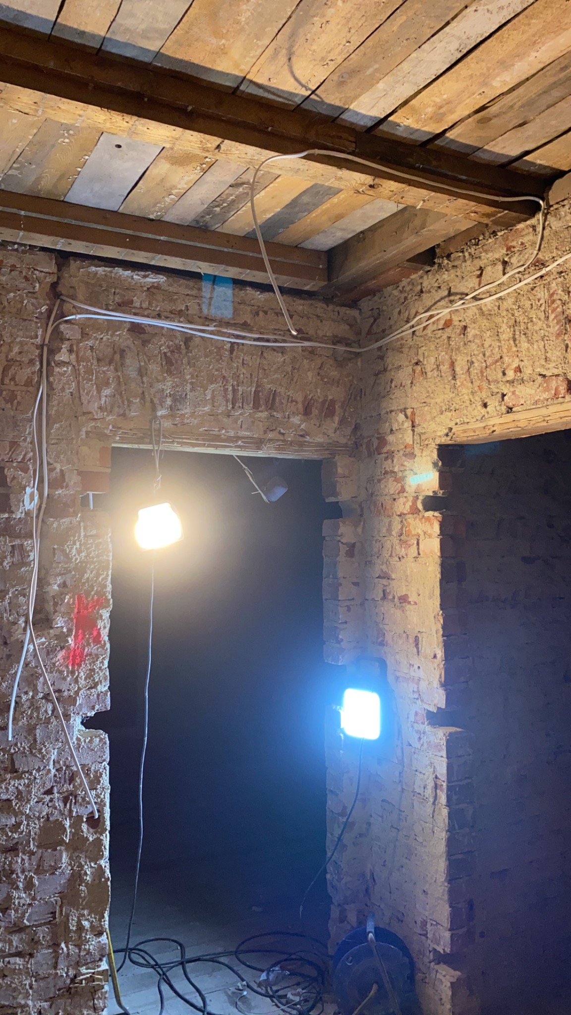 Wnętrze w trakcie remontu: surowa cegła, drewniany strop, prowizoryczne oświetlenie halogenowe, ślady po skuciu tynku i instalacji elektrycznej.