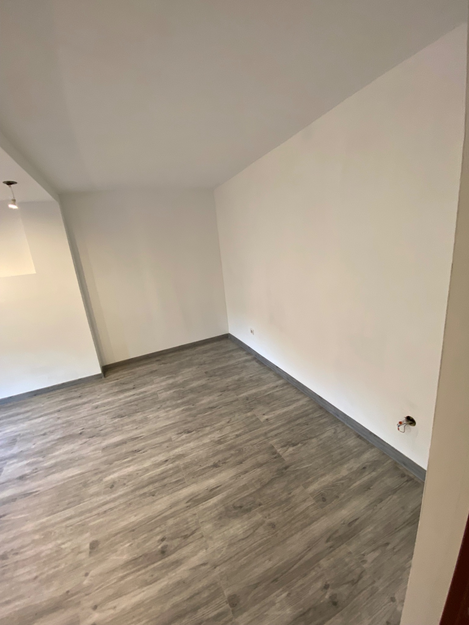 Pusty pokój po remoncie: świeżo pomalowane białe ściany, szare panele podłogowe imitujące drewno, widoczne gniazdko elektryczne bez osprzętu.