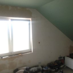 DAPO Firma Ogólnobudowlana - Poddasze w Rogoźnie w trakcie prac przygotowawczych, widoczne ślady po szpachlowaniu przy oknie, sufit częściowo pomalowany na zielono, na podłodze leżą narzędzia i materiały budowlane.