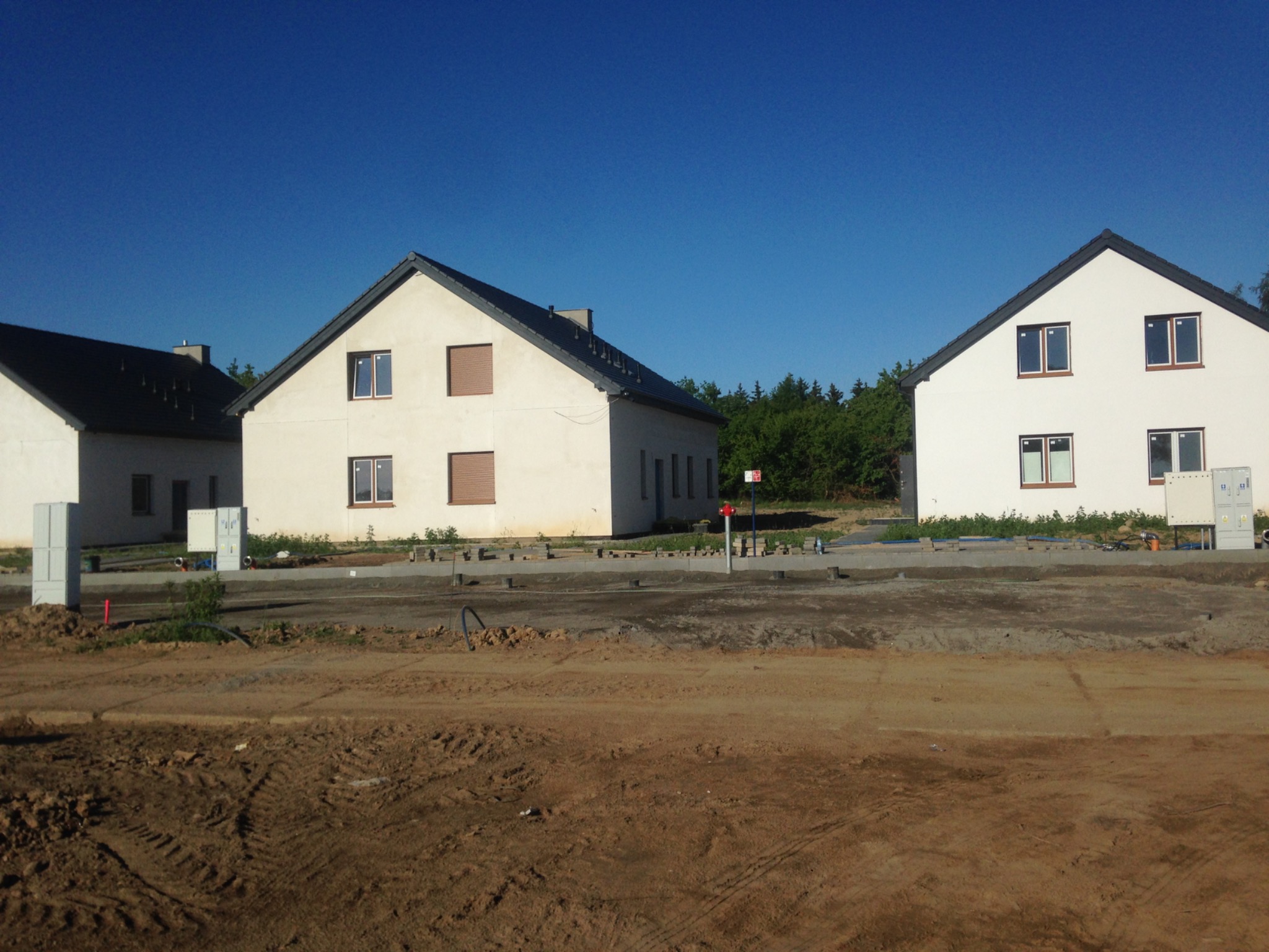 Nowe domy jednorodzinne w trakcie budowy, widoczne niedokończone elewacje i przygotowany teren.