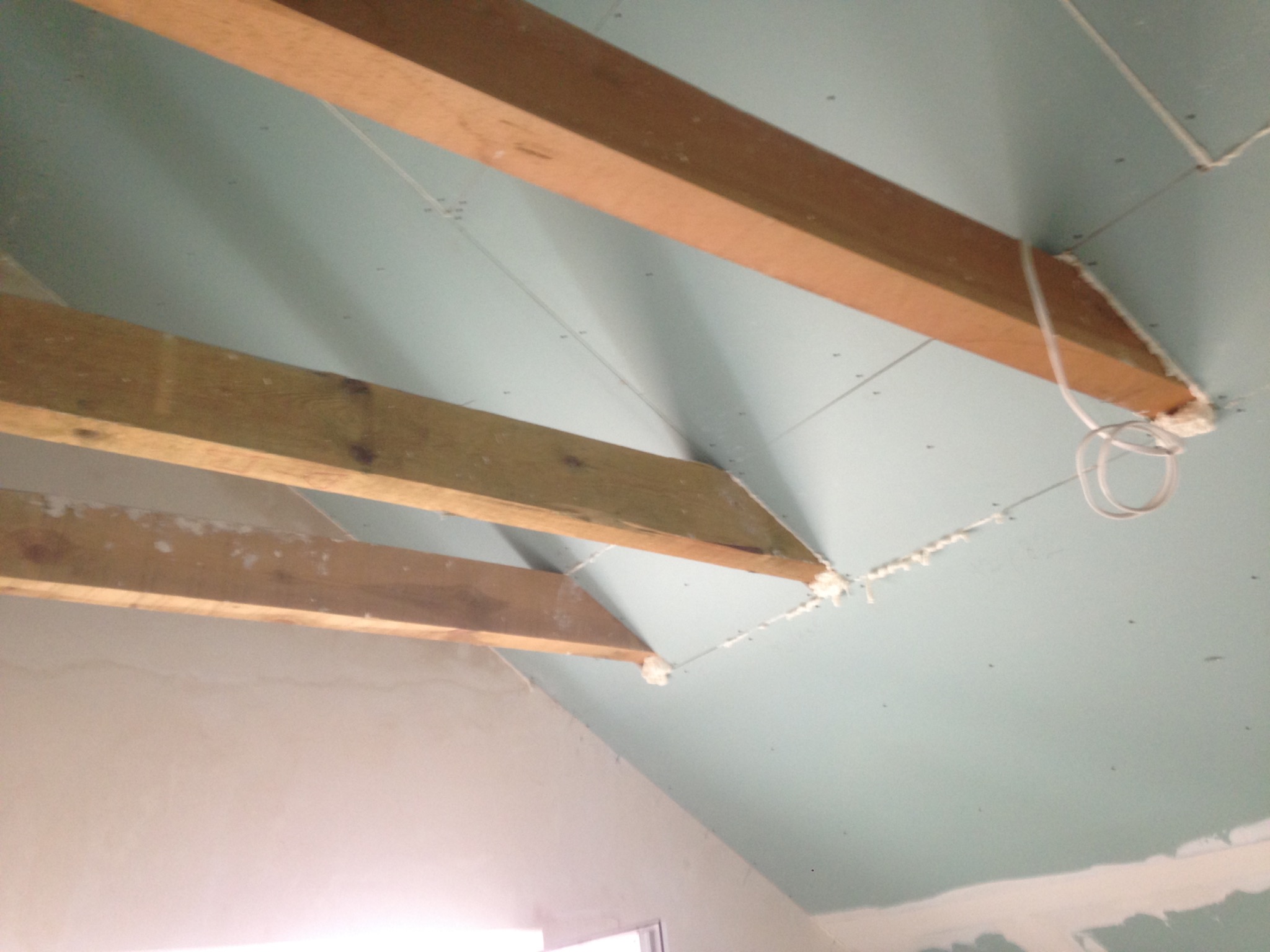 Poddasze w trakcie prac wykończeniowych: widoczne drewniane belki konstrukcyjne, płyty gipsowo-kartonowe zamontowane na skosach, szczeliny wypełnione pianką montażową oraz przewody elektryczne.