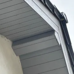 Szare podbitka dachowa z widocznymi elementami mocującymi i fragmentem ściany budynku w tle.