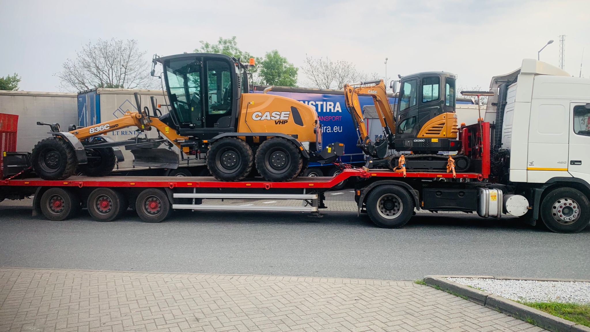 Laweta z dwoma maszynami budowlanymi marki Case, w tym równiarką i mini koparką, przygotowana do transportu na terenie Poznania. Równiarka ma oznaczenie 836C AWD, a koparka CX26C.