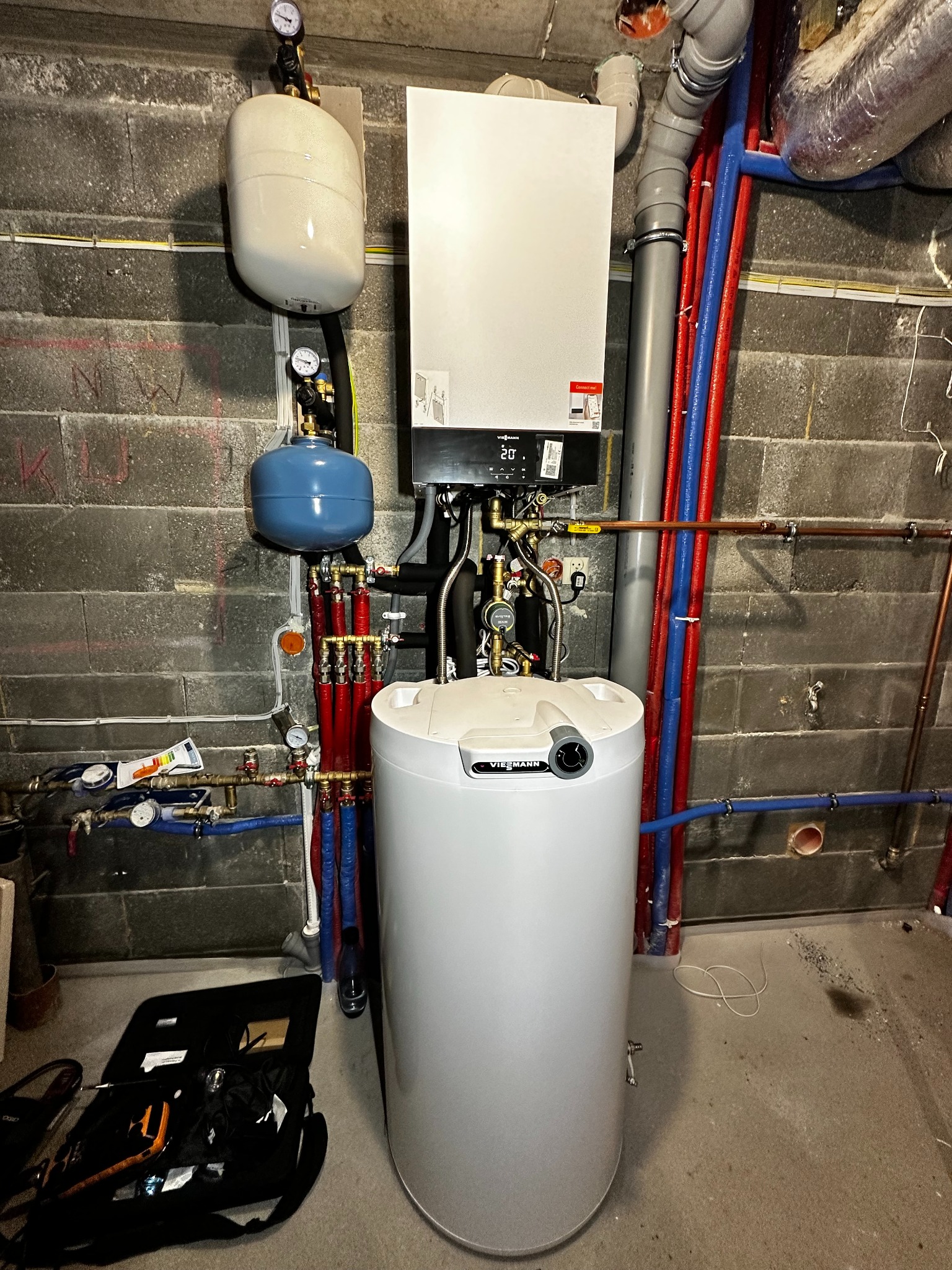 Zmontowany, nowoczesny piec gazowy Viessmann z instalacją CO w kotłowni z szarych bloczków. Widoczne rury miedziane i z tworzywa, manometry i narzędzia w torbie monterskiej.