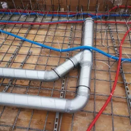 Instalacja rur wentylacyjnych z izolacją termiczną, oraz peszli elektrycznych w kolorze czerwonym i niebieskim, zamocowana na siatce zbrojeniowej na drewnianym szalunku, zabezpieczona opaskami...
