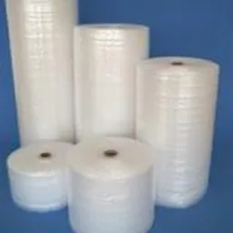 Różne rozmiary rolek białej folii pęcherzykowej na jednolitym niebieskim tle, ułożone w kompozycję od najmniejszej do największej, z widoczną strukturą pęcherzyków powietrza.