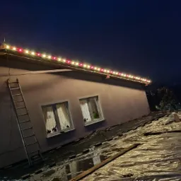 Instalacja świątecznego oświetlenia na dachu budynku w Chełmnie, widoczna drabina oparta o ścianę i folia zabezpieczająca na dachu.