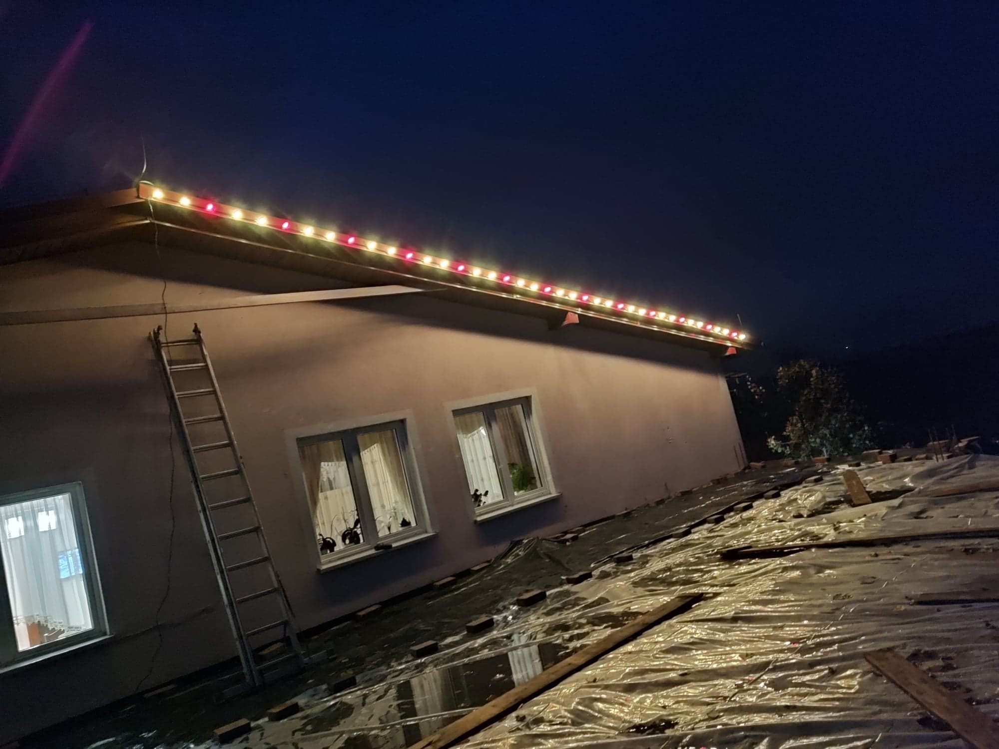 Instalacja świątecznego oświetlenia na dachu budynku w Chełmnie, widoczna drabina oparta o ścianę i folia zabezpieczająca na dachu.