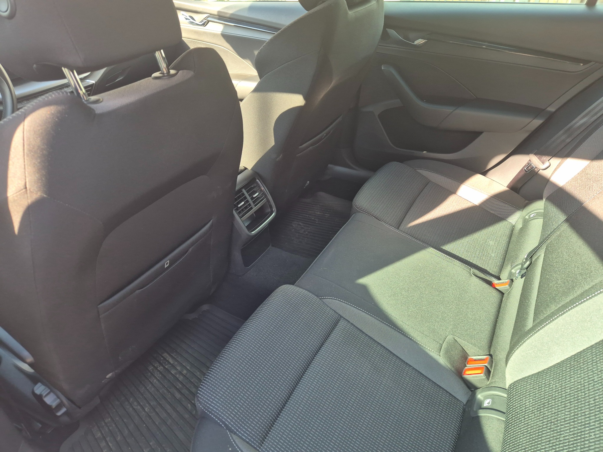 Wnętrze tylnej kanapy samochodu z widocznymi zagłówkami, pasami bezpieczeństwa i kratką nawiewu.