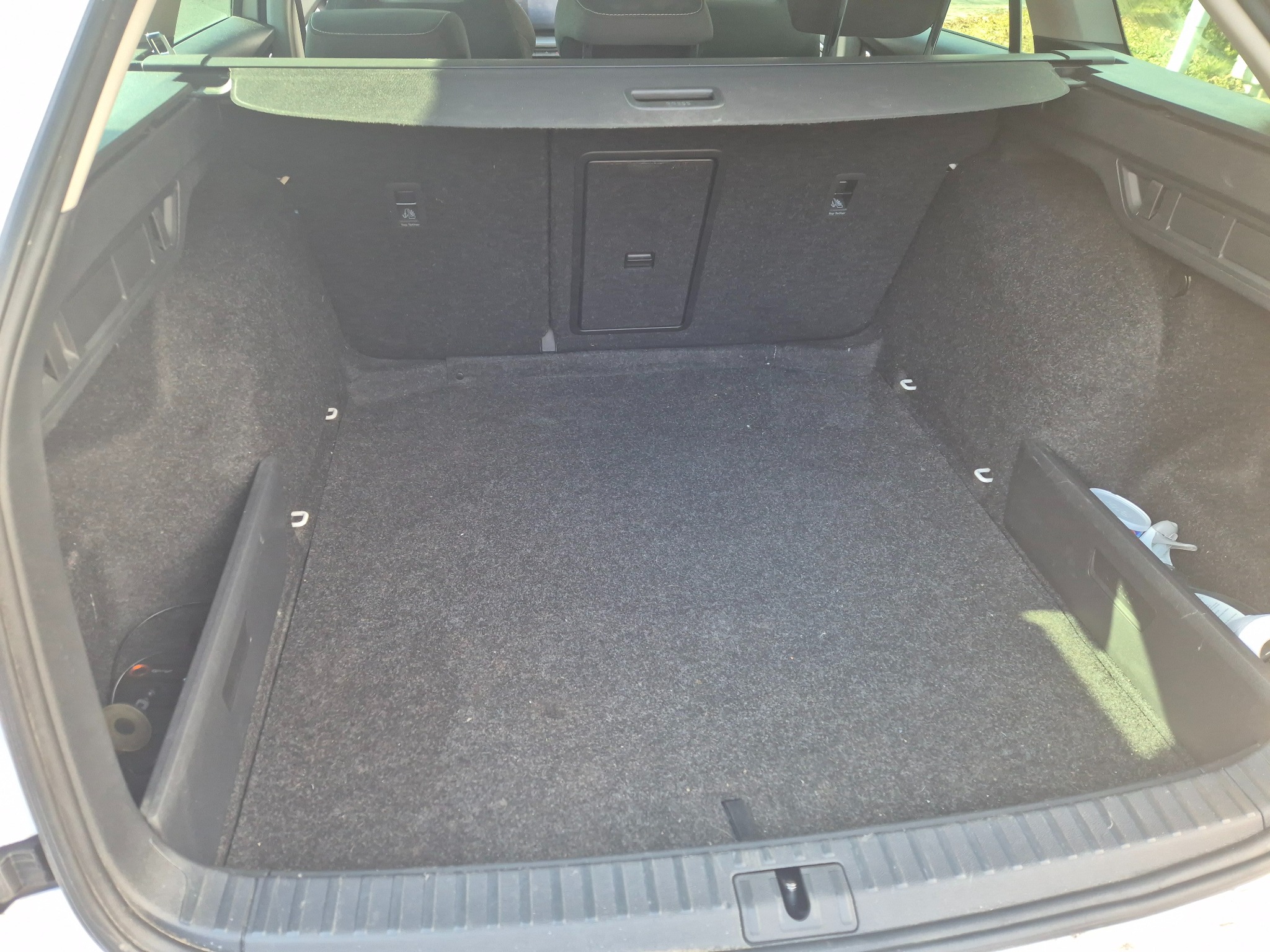 Pusta, wyłożona szarym materiałem przestrzeń bagażowa samochodu typu kombi z widoczną roletą i elementami mocującymi bagaż.