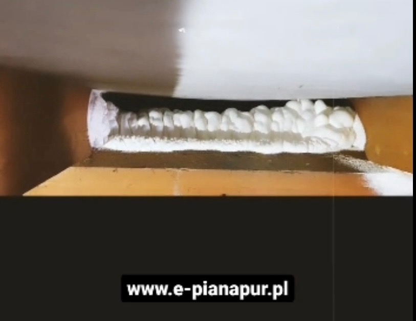 Szczelina między elementami konstrukcyjnymi wypełniona białą, spienioną substancją izolacyjną, widok z bliska.