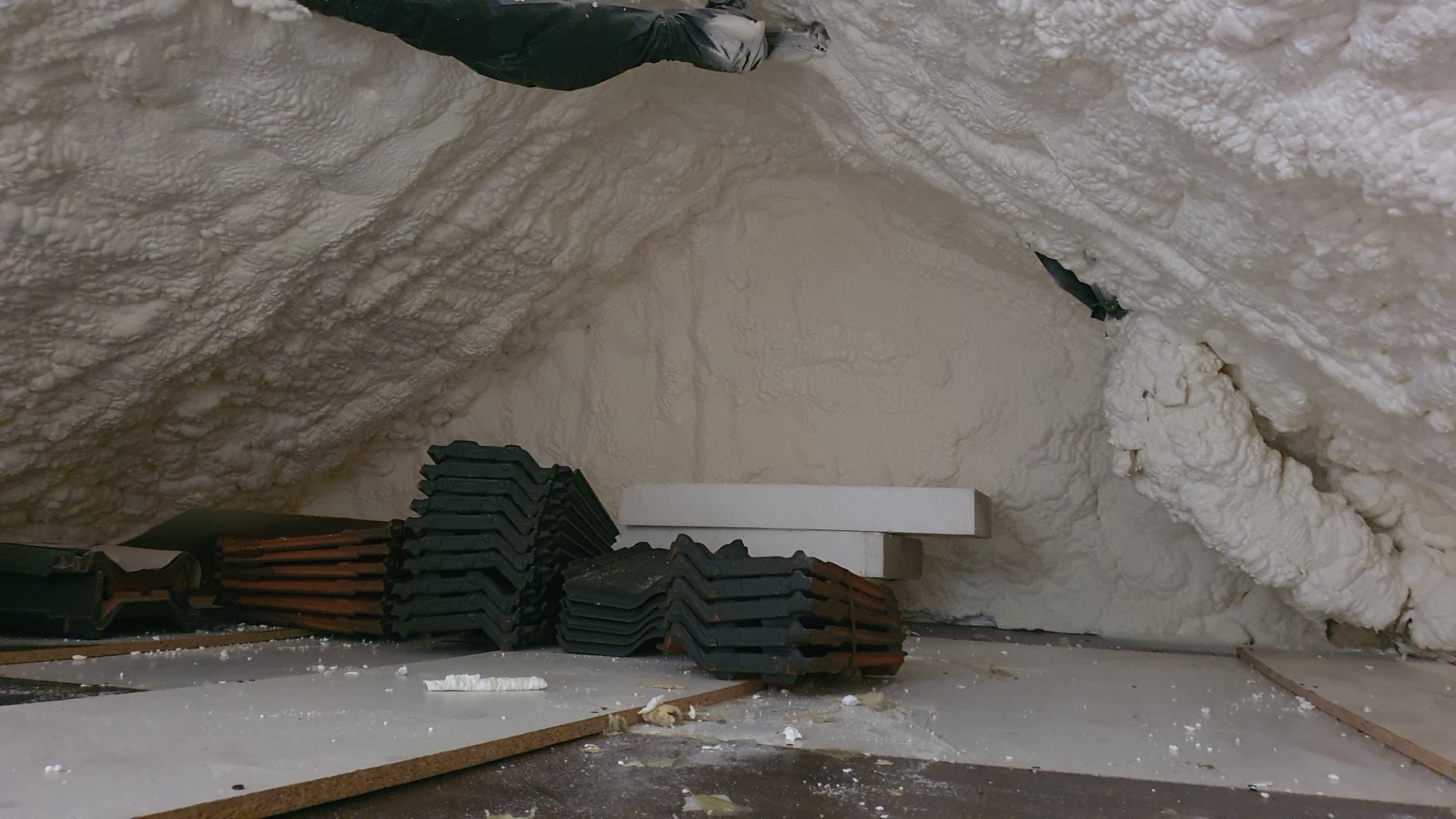 Poddasze z ociepleniem, widoczne stosy dachówek i fragmenty płyt gipsowych na podłodze.