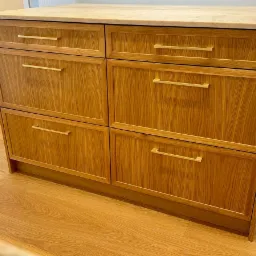 Drewniana komoda z sześcioma szufladami i marmurowym blatem, widoczna na tle okna z żaluzjami i krzesła.