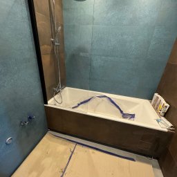 Max -Bud - Remont łazienki w toku: zabezpieczona wanna folią, widoczne płytki w odcieniach brązu i turkusu, przygotowane silikony. Podłoga zabezpieczona kartonem.