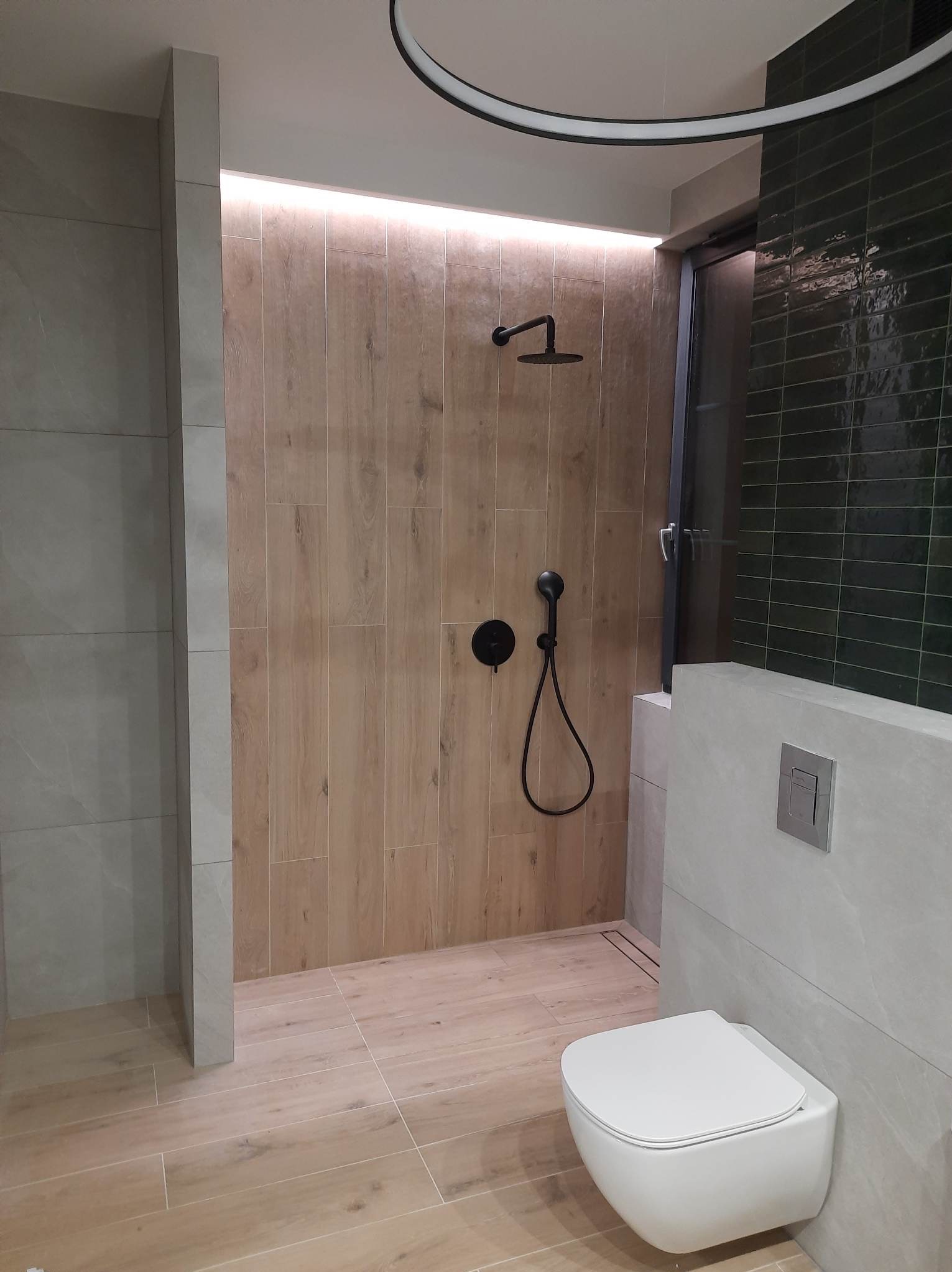 Nowoczesna łazienka z kabiną prysznicową typu walk-in, wykończona płytkami imitującymi drewno i szarym gresem. Czarna armatura i podświetlenie LED dodają elegancji.