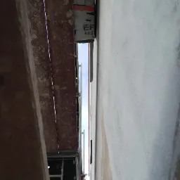 Elewacja budynku w trakcie ocieplania, widok ze szczeliny między rusztowaniem a ścianą, widoczna warstwa izolacyjna i fragment nieba.