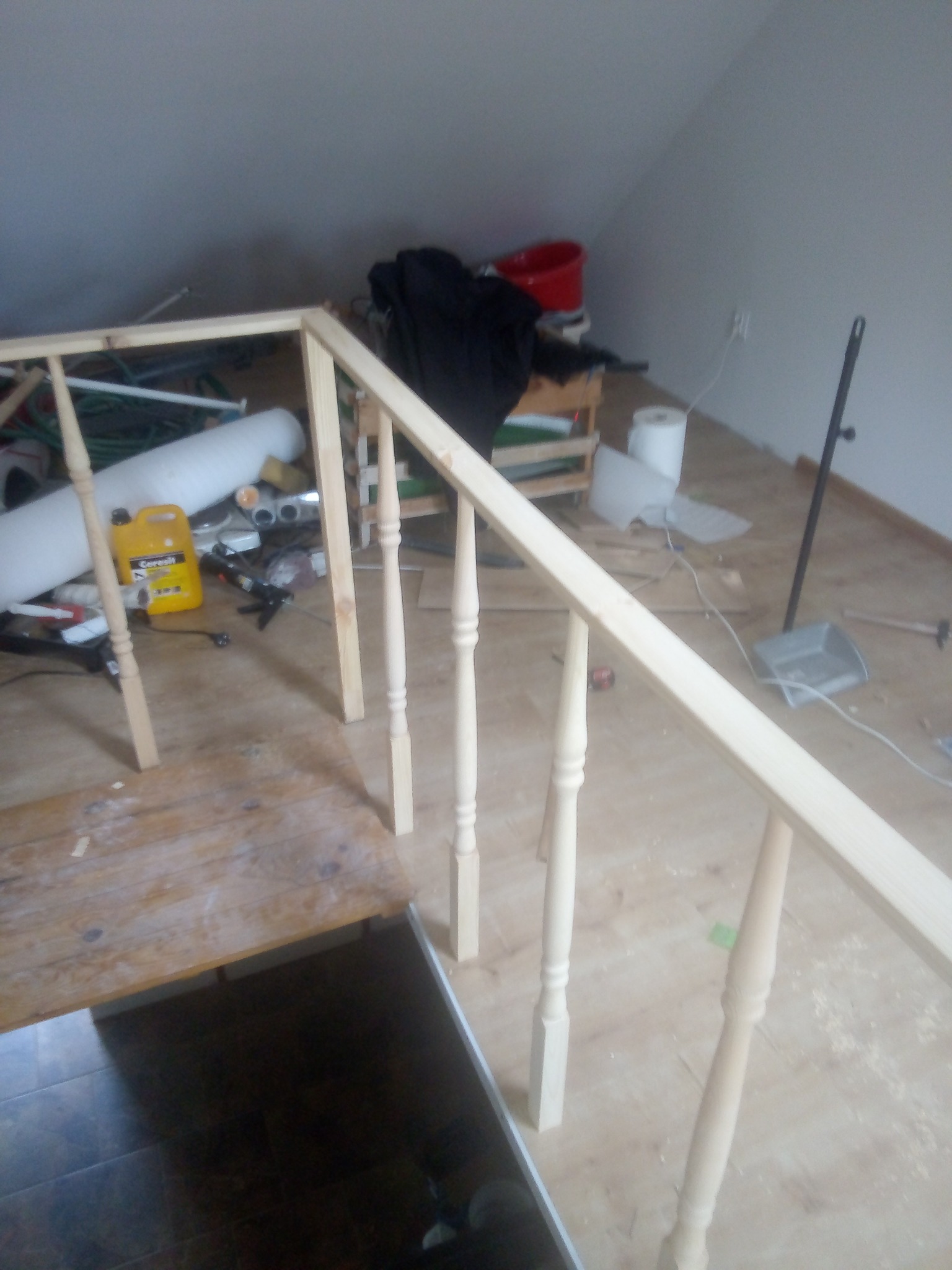 Montaż drewnianej balustrady schodowej w trakcie prac wykończeniowych, widoczne narzędzia i materiały budowlane w tle.