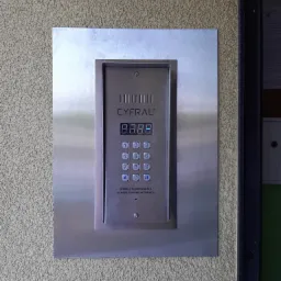 Panel domofonowy Cyfral z metalową obudową zamontowany na chropowatej ścianie budynku.
