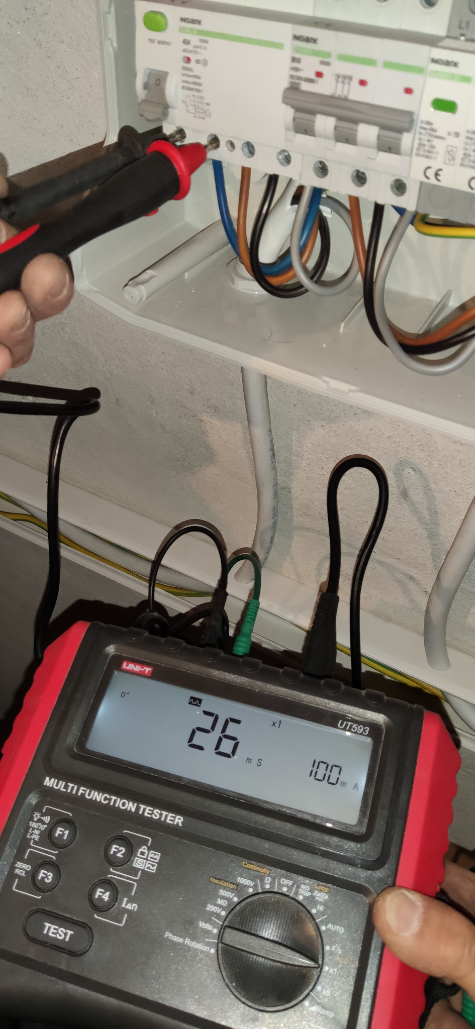 Pomiar elektryczny instalacji zabezpieczającej, widoczny multimetr UNI-T UT593 wskazujący 26 mS i 100 mA, przewody pomiarowe podłączone do bezpieczników w rozdzielni.