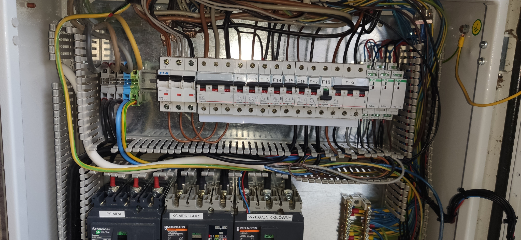 Otwarta szafa sterownicza z widocznymi zabezpieczeniami, przewodami i elementami sterującymi oznaczonymi jako 'Pompa', 'Kompresor' i 'Wyłącznik Główny'.