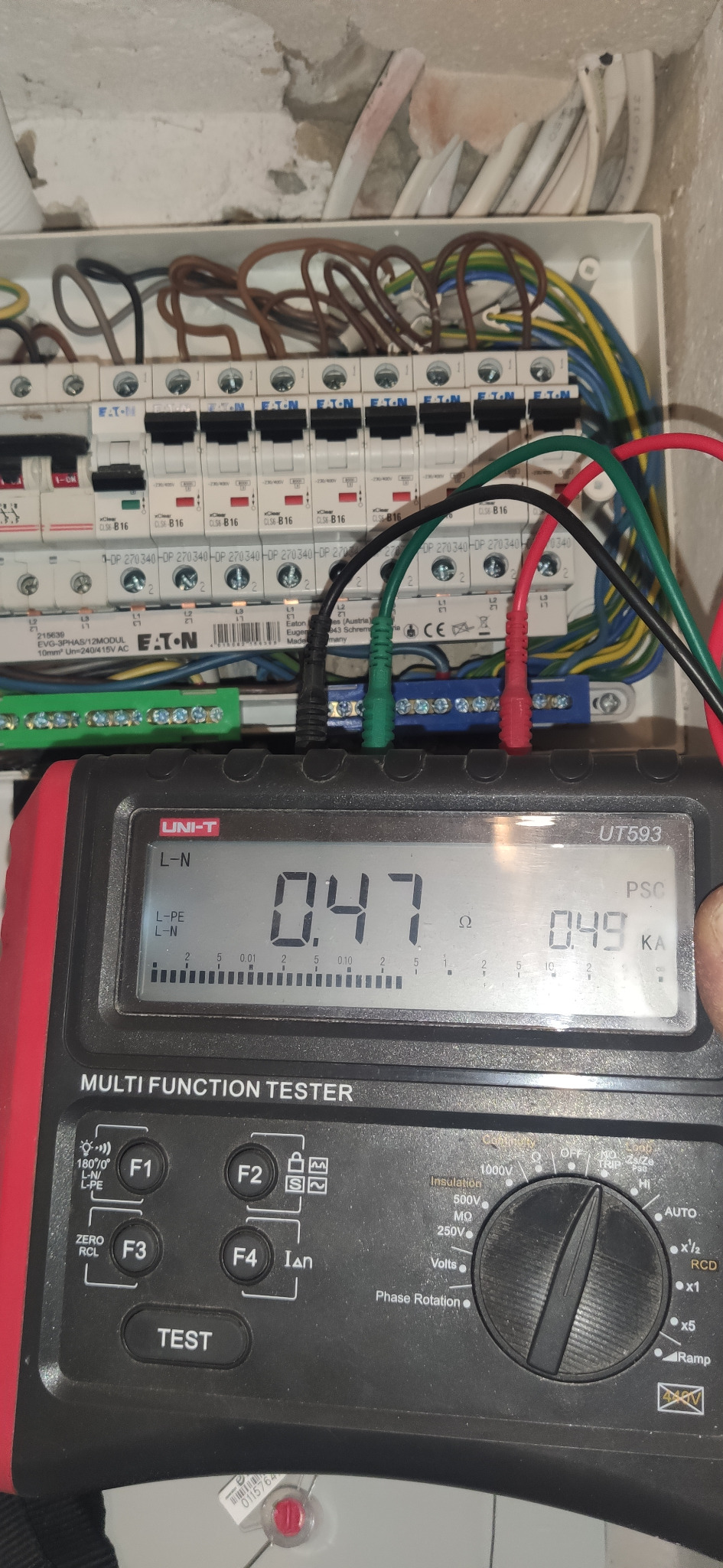 Pomiar rezystancji pętli zwarcia w rozdzielnicy elektrycznej za pomocą miernika wielofunkcyjnego Uni-T UT593, z widocznymi bezpiecznikami Eaton i przewodami pomiarowymi.