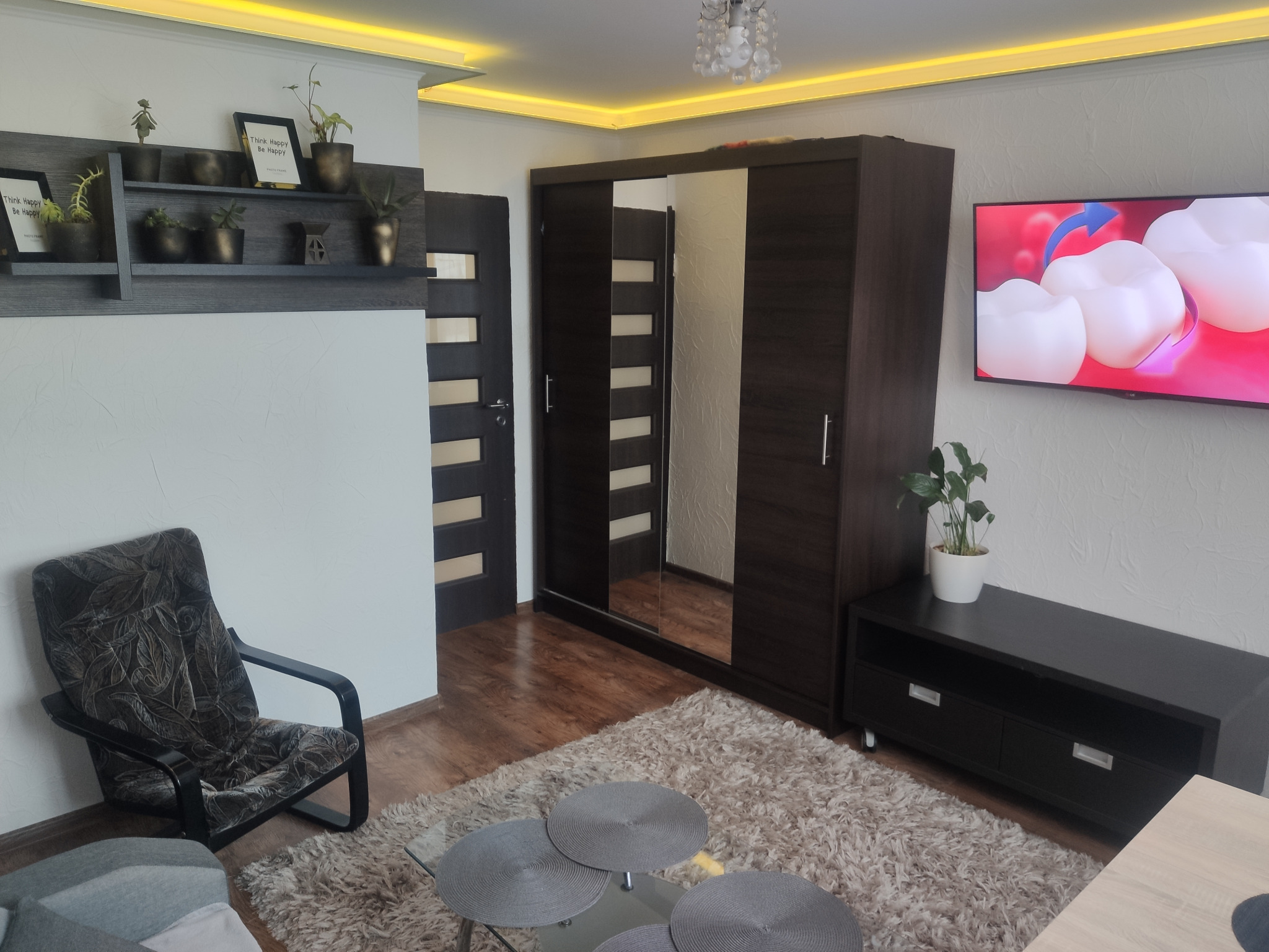 Nowoczesne wnętrze pokoju z ciemnymi meblami, puszystym dywanem, szklanym stolikiem kawowym i telewizorem z animacją 3D zębów.