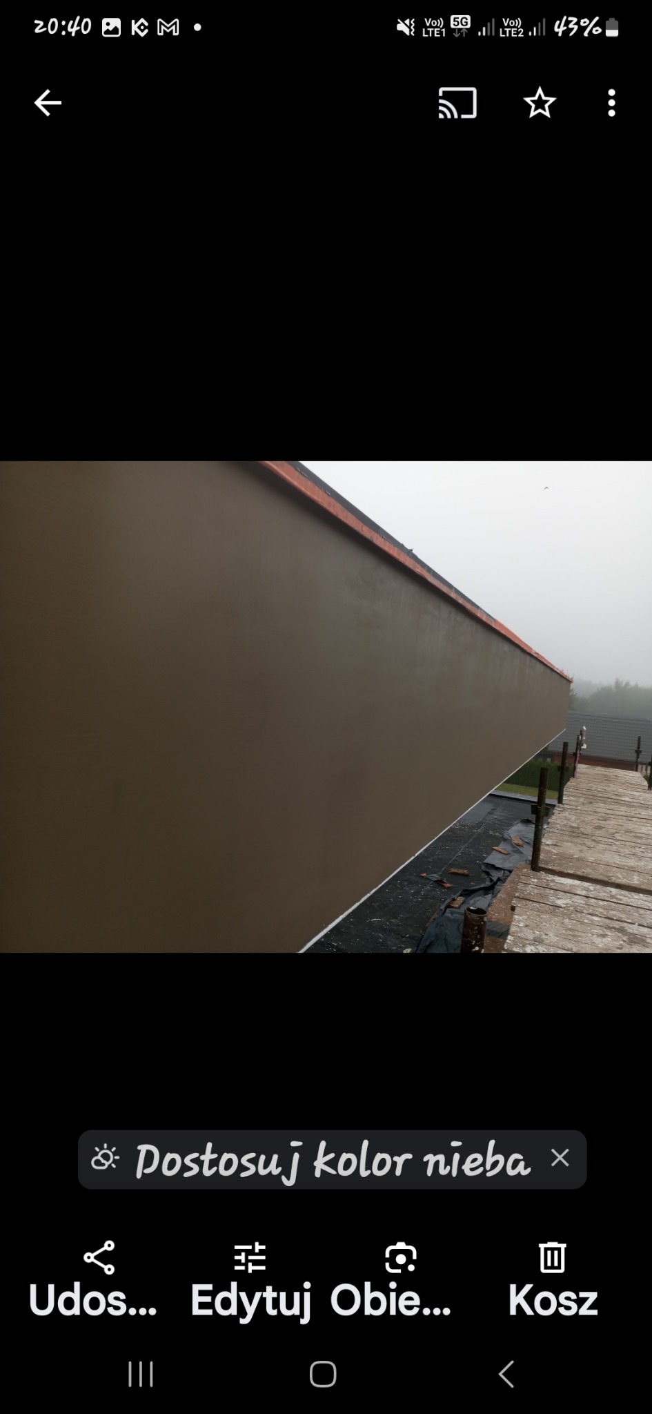 Świeżo pomalowana, beżowa elewacja budynku jednorodzinnego w pochmurny dzień, widoczna z drewnianego rusztowania.