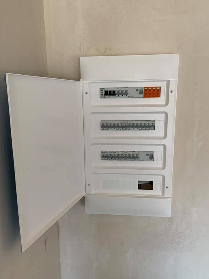 Otwarta, biała skrzynka rozdzielcza z bezpiecznikami zamontowana na surowej ścianie w Nowogardzie, widoczne cztery rzędy aparatury modułowej.