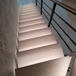 Nowoczesne schody z jasnego drewna z podświetleniem LED i czarną metalową balustradą, widok z góry.