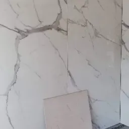 Ściana wyłożona płytami imitującymi marmur z czarną listwą wykończeniową, na podłodze pomarańczowa mata izolacyjna, oparta o ścianę płyta do montażu