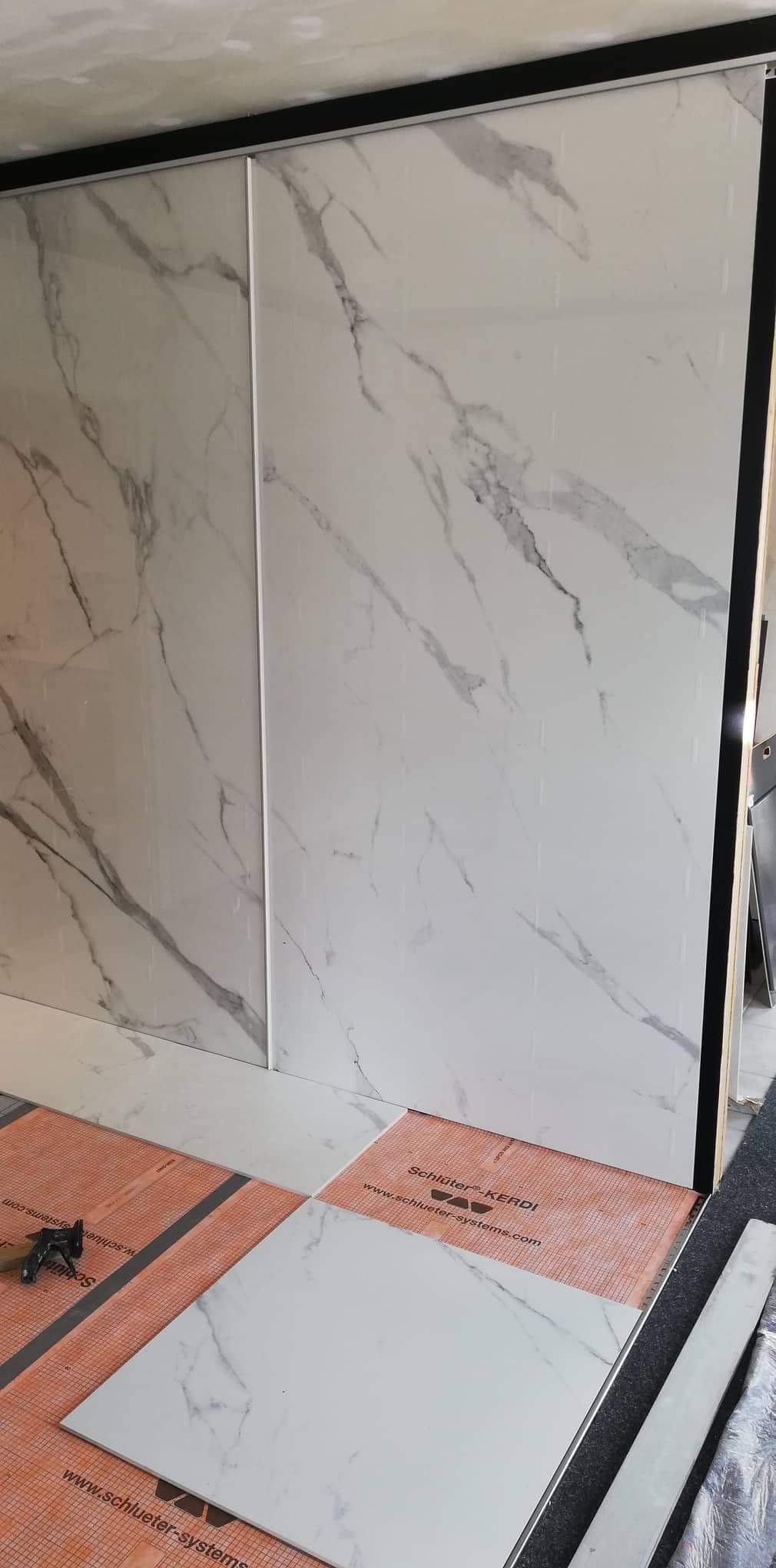 Montaż białych, marmurkowych płytek ściennych i podłogowych na pomarańczowej membranie hydroizolacyjnej Schluter Kerdi, widoczne narzędzia glazurnicze.