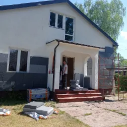 Ocieplanie ściany domu styropianem grafitowym, widoczne rusztowanie i materiały budowlane Arsanit Thermo Lambda 31.