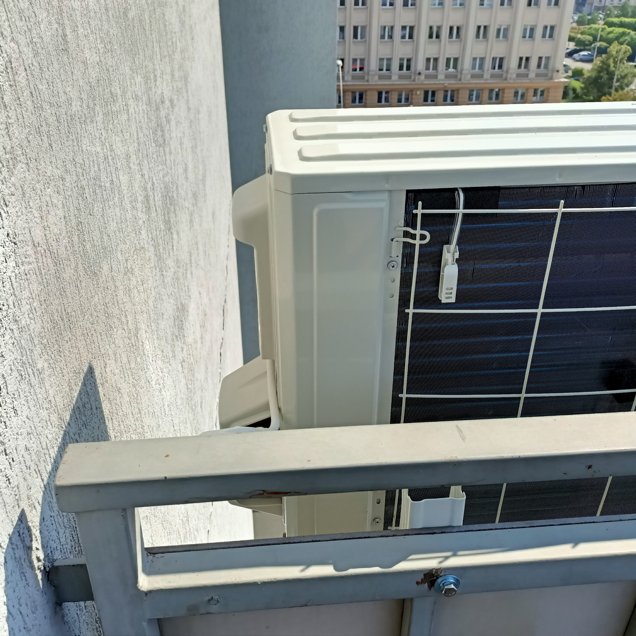 Zewnętrzna jednostka klimatyzacji zamontowana na balkonie w Krosno, widok z boku, z widocznym budynkiem w tle.