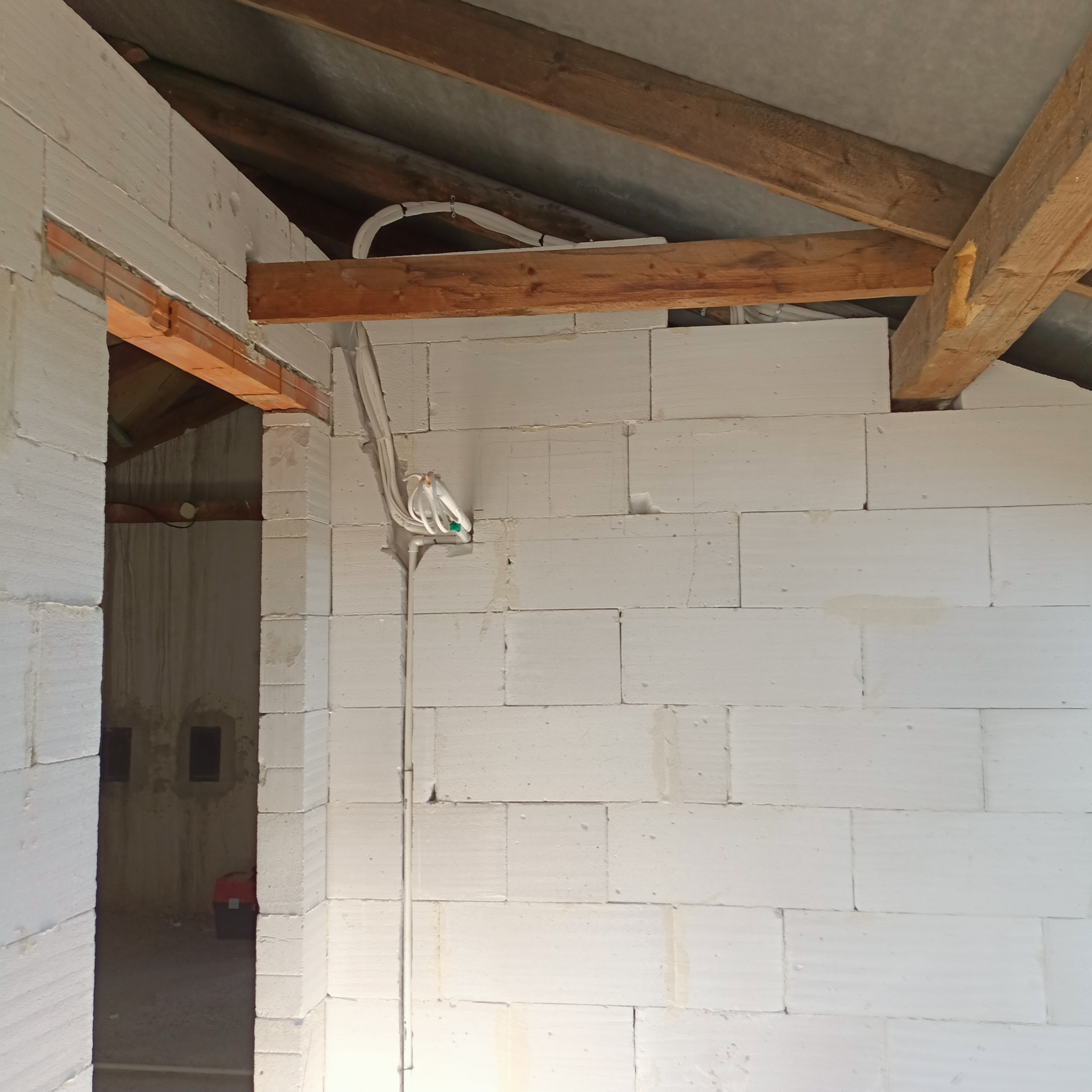 Wnętrze budynku w trakcie budowy, ściany z białych bloczków, drewniana konstrukcja dachu, widoczne przewody elektryczne w peszlu.