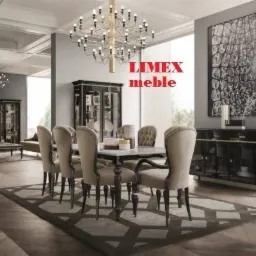 Elegancka jadalnia z owalnym stołem i krzesłami tapicerowanymi w beżowej tkaninie, oświetlona dekoracyjnym żyrandolem, z czarną komodą i abstrakcyjnym obrazem w tle.